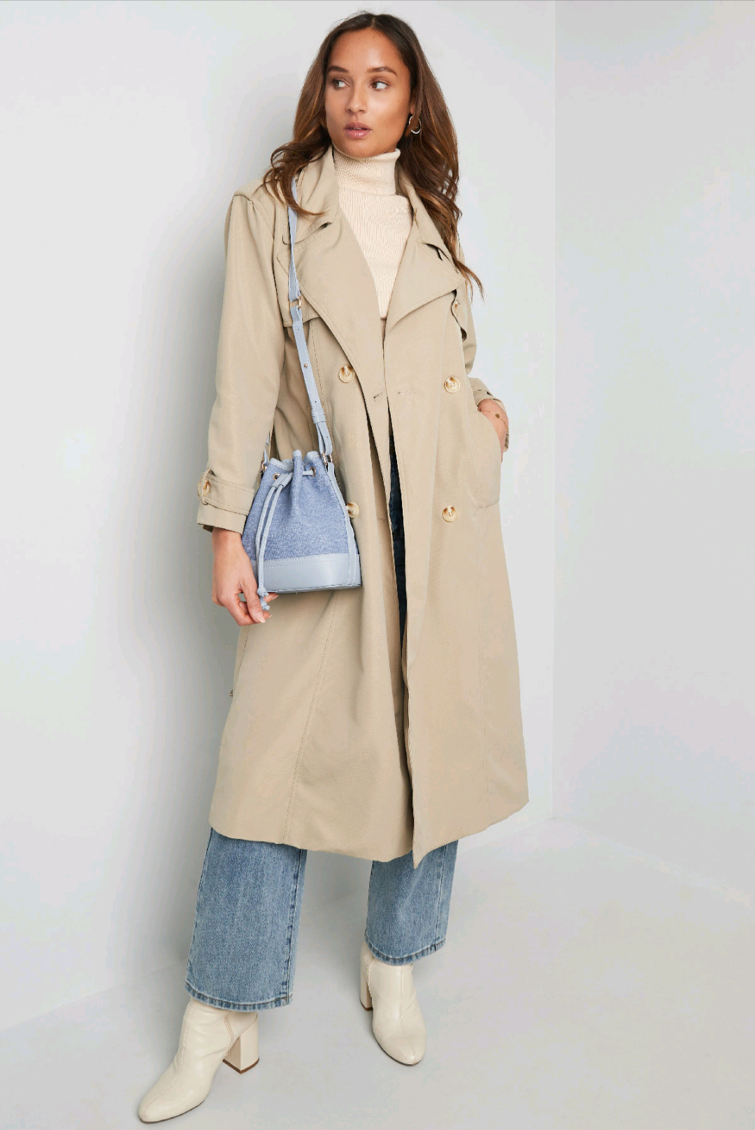 Bucketbag dames - lichtblauw denim in combinatie met beige trenchcoat en lichtblauwe spijkerbroek voor casual look.